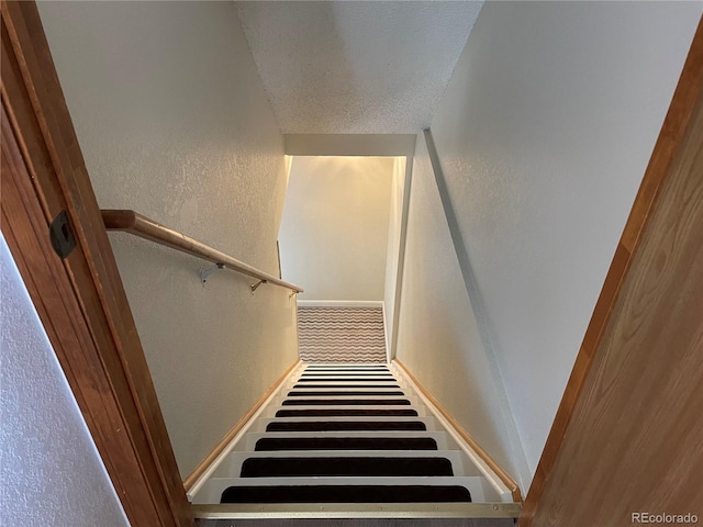stairway featuring a textured wall, a textured ceiling, and baseboards
