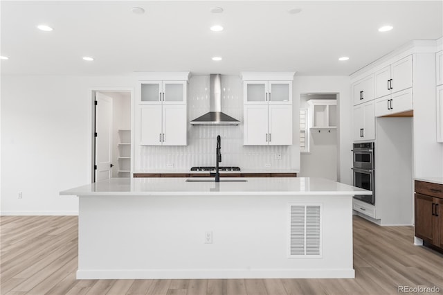 8850 Moonshimmer Trl, Littleton, CO 80125 - kitchen with wall chimney exhaust hood, tasteful backsplash, an island with sink, light countertops, and white cabinets