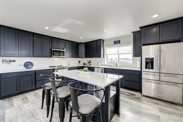 kitchen with appliances with stainless steel finishes, sink, a breakfast bar area, a center island, and light hardwood / wood-style floors