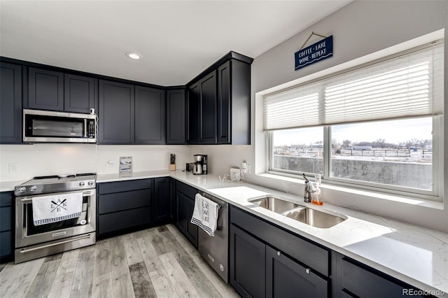 kitchen with appliances with stainless steel finishes, sink, light stone counters, and light hardwood / wood-style flooring