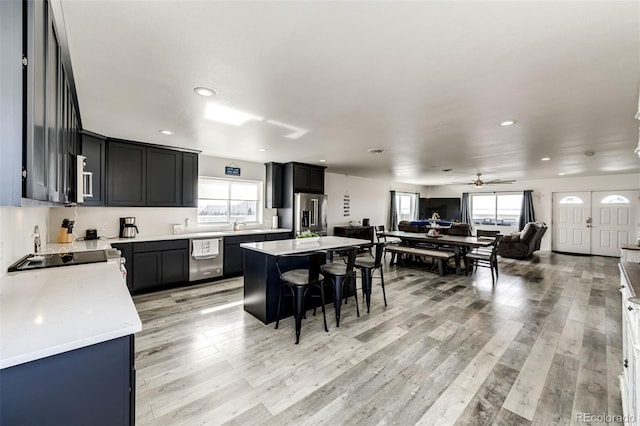 kitchen with a kitchen bar, a center island, ceiling fan, stainless steel appliances, and light hardwood / wood-style flooring