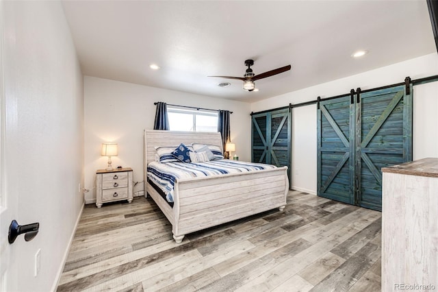 bedroom with wood-type flooring, a barn door, and ceiling fan