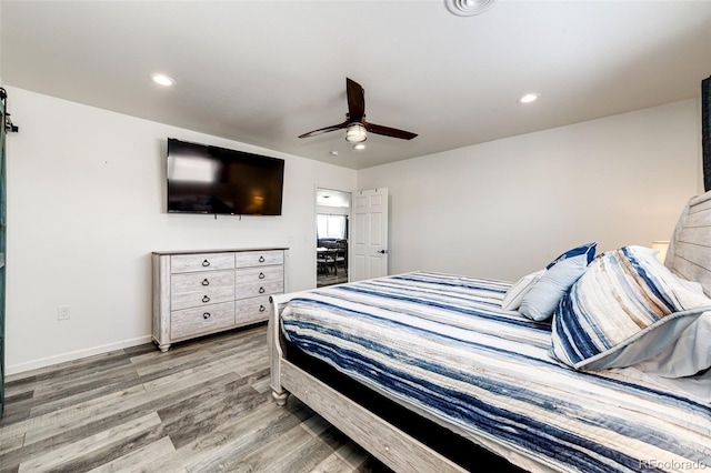 bedroom featuring ceiling fan, a barn door, and light wood-type flooring