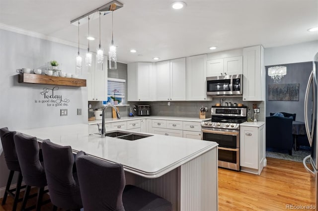 kitchen featuring appliances with stainless steel finishes, pendant lighting, white cabinetry, sink, and kitchen peninsula