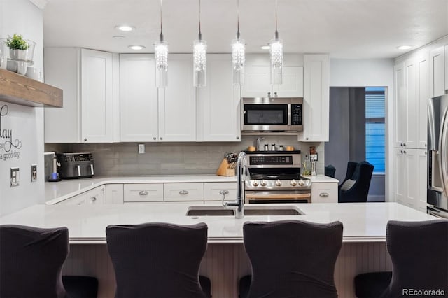 kitchen featuring pendant lighting, a breakfast bar, appliances with stainless steel finishes, white cabinets, and decorative backsplash