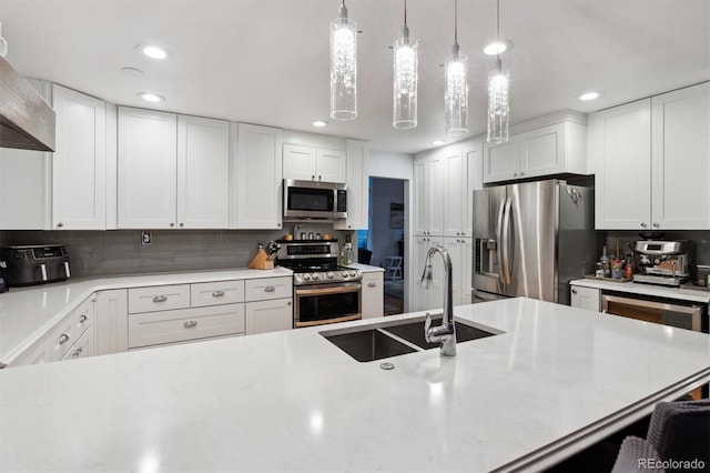 kitchen featuring wall chimney exhaust hood, sink, pendant lighting, stainless steel appliances, and white cabinets