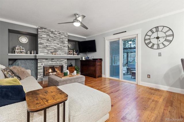 living room with crown molding, a large fireplace, wood-type flooring, and ceiling fan