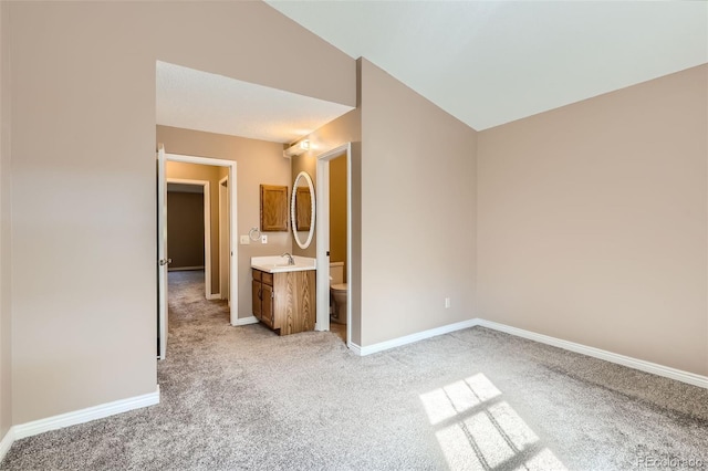 unfurnished bedroom featuring light colored carpet, ensuite bathroom, sink, and lofted ceiling