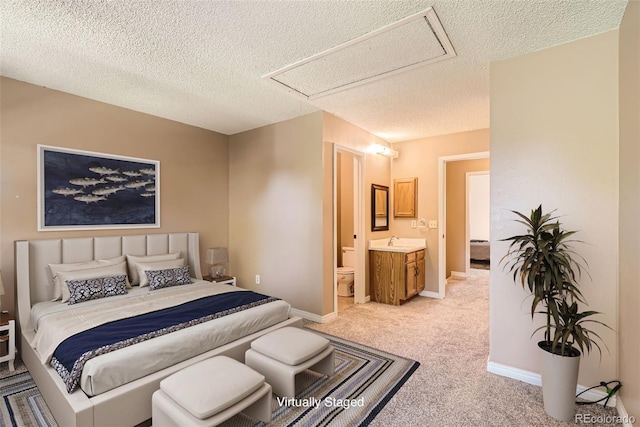 carpeted bedroom with ensuite bathroom, sink, and a textured ceiling