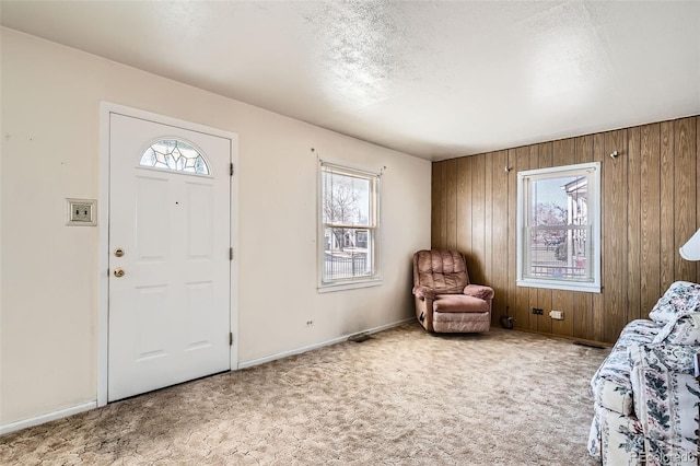 carpeted entrance foyer featuring wood walls, a textured ceiling, and baseboards