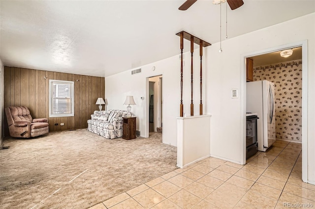 unfurnished room with visible vents, wooden walls, light carpet, light tile patterned floors, and a ceiling fan