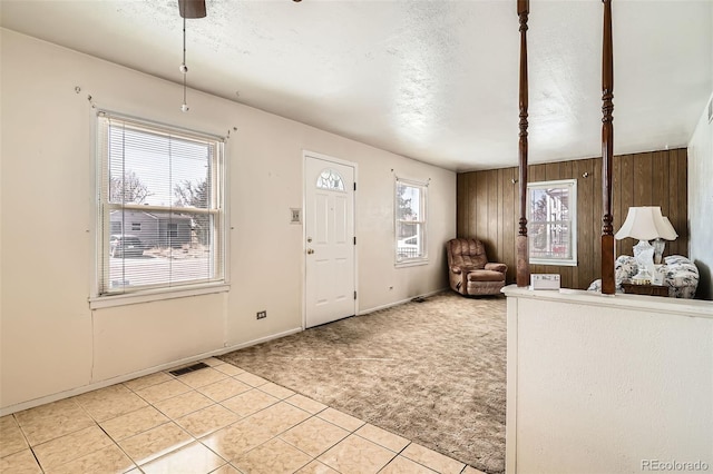 entrance foyer with visible vents, light tile patterned flooring, wood walls, a textured ceiling, and light colored carpet