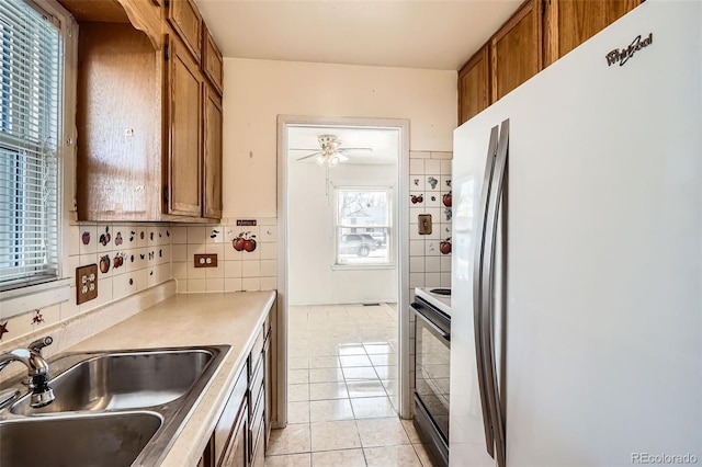 kitchen with electric range, brown cabinets, a sink, tasteful backsplash, and freestanding refrigerator