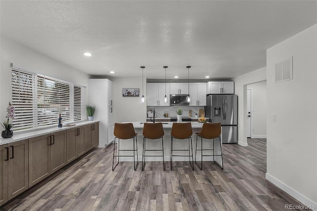 kitchen with visible vents, wood finished floors, a center island with sink, a kitchen bar, and stainless steel fridge