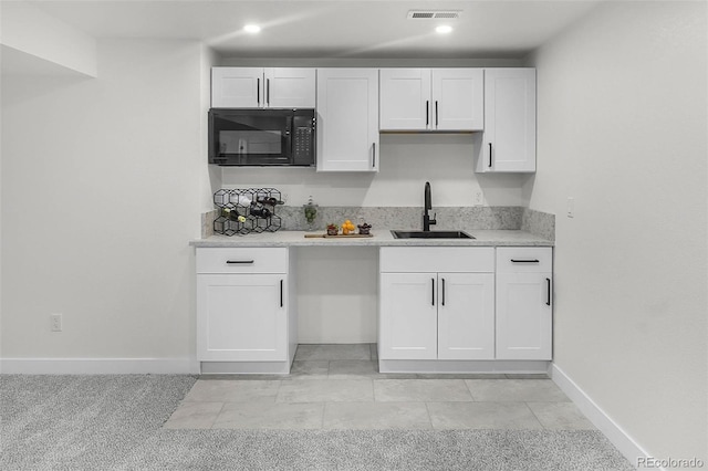 kitchen with visible vents, black microwave, baseboards, white cabinets, and a sink
