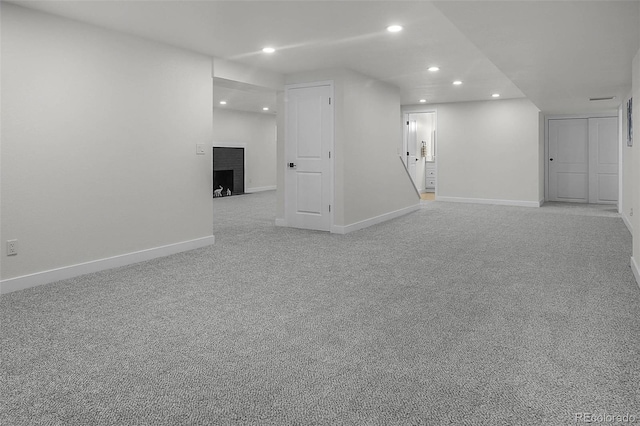 finished basement with baseboards, light carpet, a brick fireplace, and recessed lighting