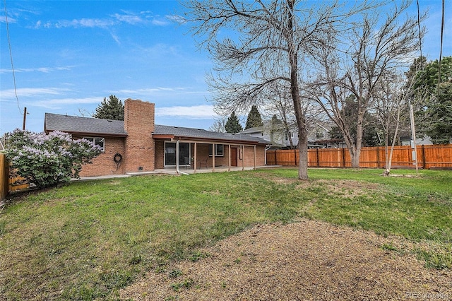 rear view of property with a chimney, a lawn, a patio area, brick siding, and a fenced backyard