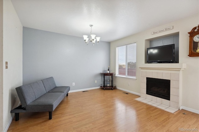 sitting room with a tiled fireplace, a chandelier, and light wood-type flooring