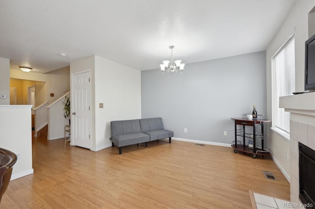 sitting room with a wealth of natural light, a tile fireplace, an inviting chandelier, and light wood-type flooring