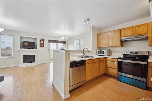 kitchen featuring appliances with stainless steel finishes, sink, a chandelier, light hardwood / wood-style flooring, and a tiled fireplace