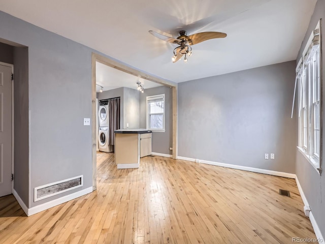 unfurnished living room featuring ceiling fan, stacked washer and clothes dryer, and light hardwood / wood-style flooring