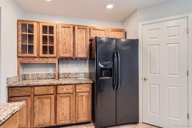 8750 Redwing Ave, Littleton, CO 80126 - kitchen with black fridge with ice dispenser, glass insert cabinets, light stone counters, and brown cabinets