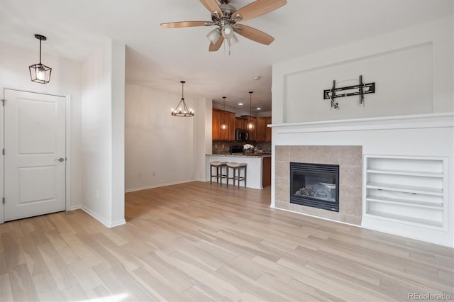 unfurnished living room featuring recessed lighting, a tile fireplace, baseboards, light wood-style flooring, and ceiling fan with notable chandelier