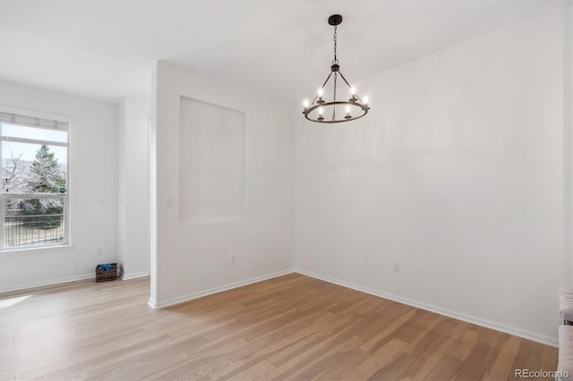 spare room featuring a chandelier, light wood finished floors, and baseboards