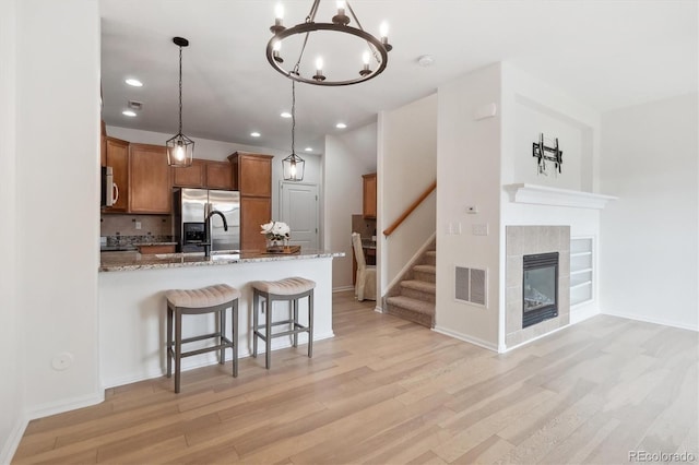 kitchen featuring a peninsula, stainless steel appliances, light wood-type flooring, visible vents, and brown cabinetry