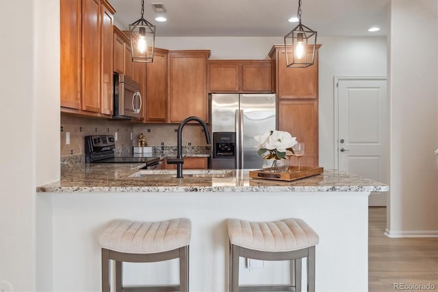 kitchen with brown cabinets, a peninsula, appliances with stainless steel finishes, and light stone counters
