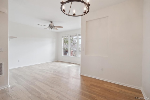 spare room with light wood-style floors, visible vents, baseboards, and ceiling fan with notable chandelier