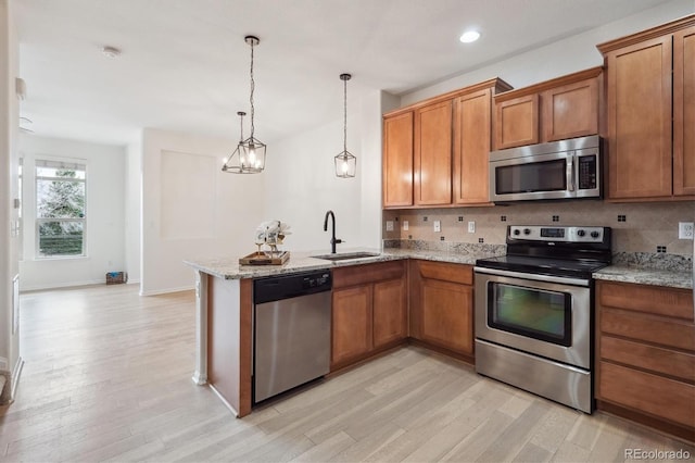 kitchen featuring a sink, brown cabinets, stainless steel appliances, light wood-style flooring, and a peninsula