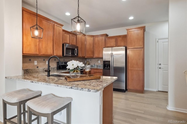 kitchen with a peninsula, light wood-style floors, brown cabinets, light stone countertops, and appliances with stainless steel finishes