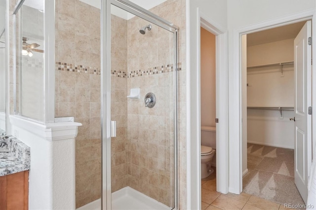 bathroom featuring a spacious closet, tile patterned floors, toilet, a ceiling fan, and a stall shower