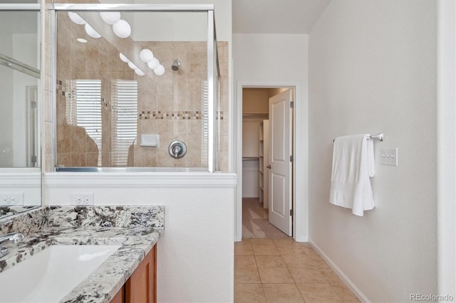 bathroom featuring tile patterned flooring, vanity, a walk in closet, baseboards, and tiled shower