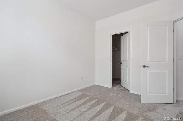 unfurnished bedroom with a spacious closet, baseboards, and light carpet