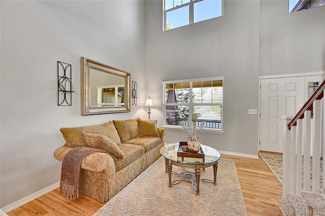 living room with baseboards, plenty of natural light, light wood finished floors, and a towering ceiling