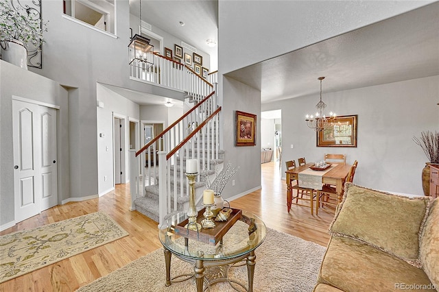living area with an inviting chandelier, stairway, wood finished floors, and a towering ceiling