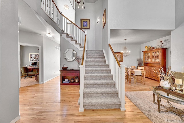 stairs with baseboards, a towering ceiling, wood finished floors, and a notable chandelier
