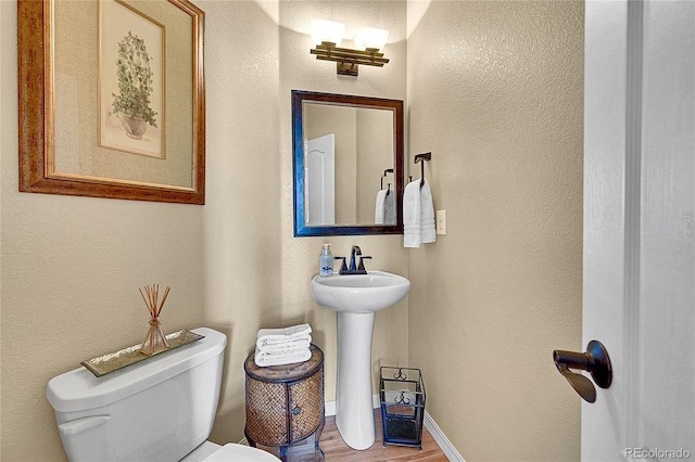 bathroom with baseboards, a textured wall, wood finished floors, and toilet