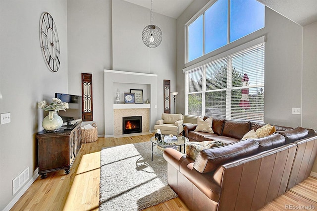 living room with high vaulted ceiling, baseboards, a fireplace with flush hearth, wood finished floors, and visible vents