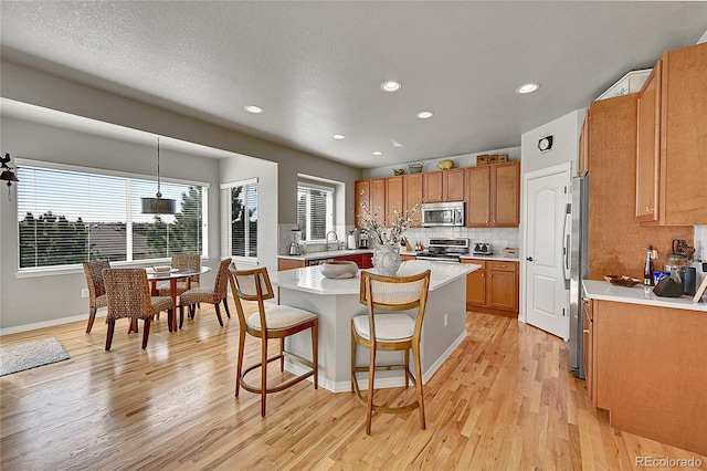 kitchen with appliances with stainless steel finishes, light countertops, a kitchen breakfast bar, light wood-style flooring, and a center island