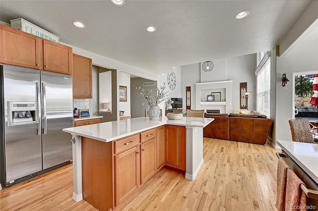 kitchen with light countertops, stainless steel refrigerator with ice dispenser, open floor plan, and light wood finished floors