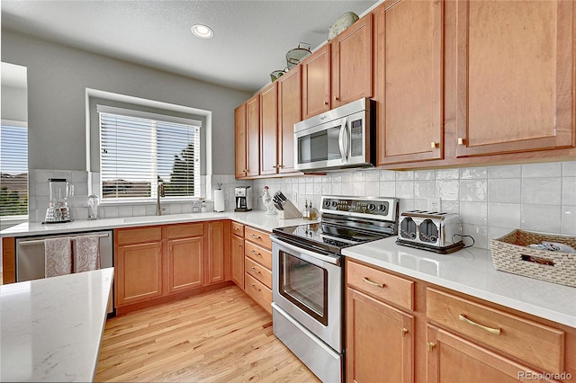 kitchen with a sink, light wood-style floors, stainless steel appliances, recessed lighting, and backsplash