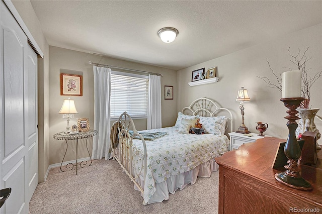bedroom with a textured ceiling, light carpet, baseboards, and a closet