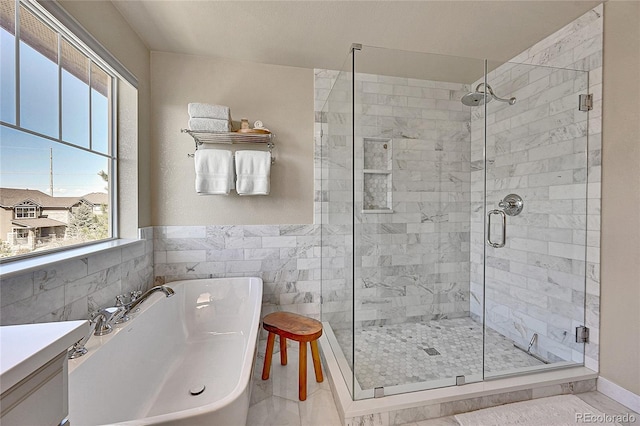 bathroom with a shower stall, wainscoting, a freestanding bath, and tile walls