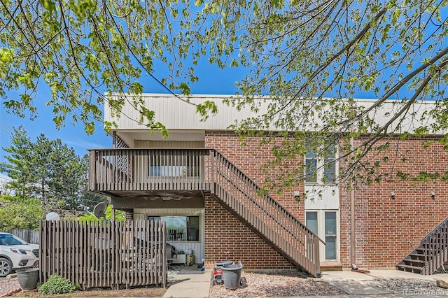 rear view of property featuring stairs, fence, and brick siding
