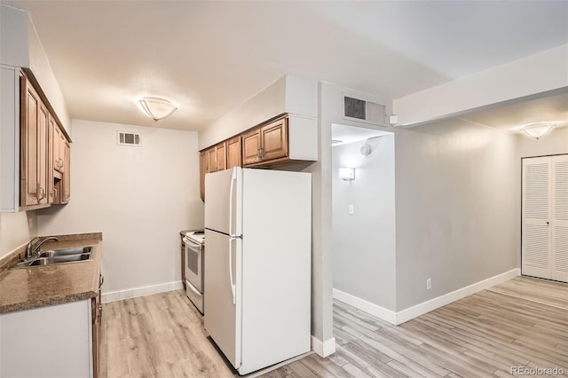 kitchen with white appliances, a sink, light wood-type flooring, and baseboards