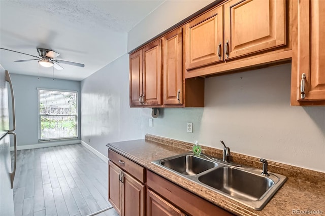 kitchen featuring a sink, baseboards, a ceiling fan, freestanding refrigerator, and wood finished floors
