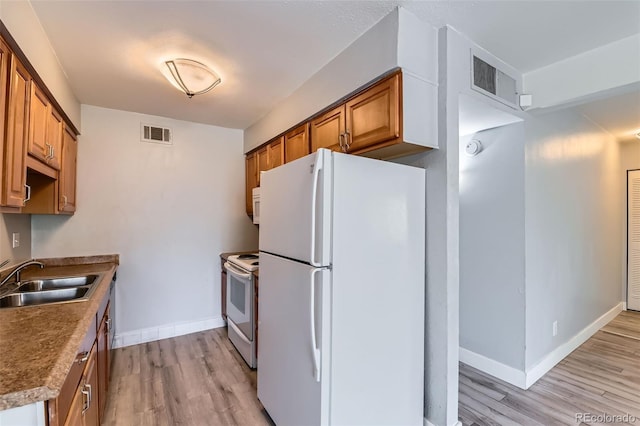 kitchen with white appliances, a sink, light wood finished floors, and baseboards